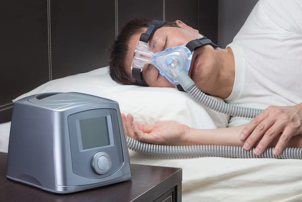 Asian man with sleep apnea using CPAP machine, wearing headgear mask connecting to air tube