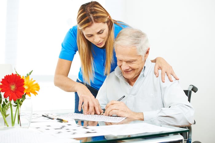 Senior man in wheelchair solving mazes as memory training with help of daughter