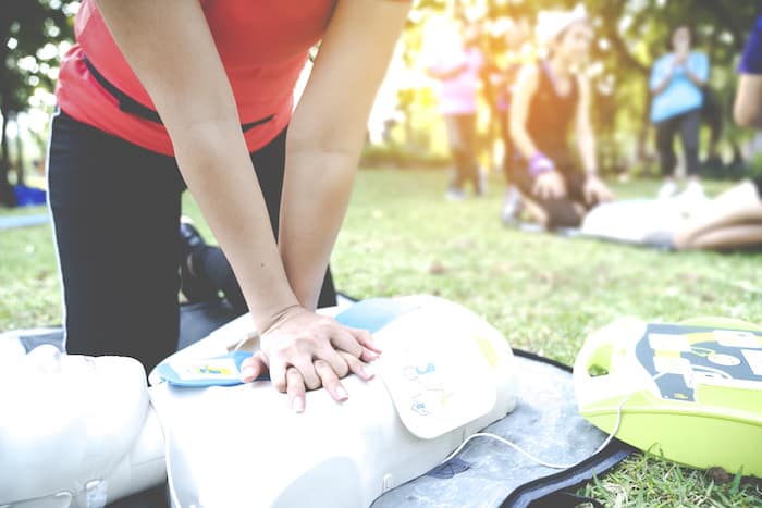 Asian female or runner woman training CPR demonstrating in park by put hands and interlock finger over CPR doll give chest compression. First aid training for heart attack people or lifesaver.