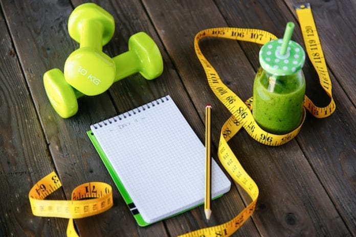 Detox green smoothie, blank copyspace notebook and measuring tape on wooden table for dieting and healthy fitness nutrition concept. Workout routine and diet planning.