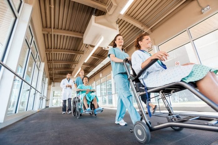 Low angle view of female nurses pushing patients on wheelchairs with doctor walking at corridor in hospital