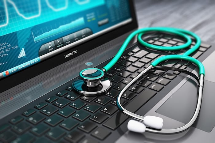 Creative abstract healthcare, medicine and cardioloagy tool concept: laptop or notebook computer PC with medical cardiologic diagnostic test software on screen and stethoscope on black wooden business office table with selective focus effect