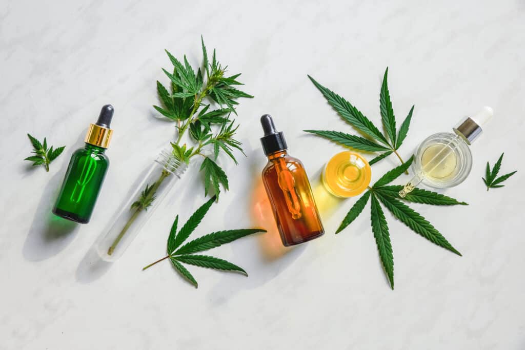 Different glass bottles with CBD OIL, THC tincture and cannabis leaves on yellow background. Flat lay, minimalism. Cosmetics CBD oil.