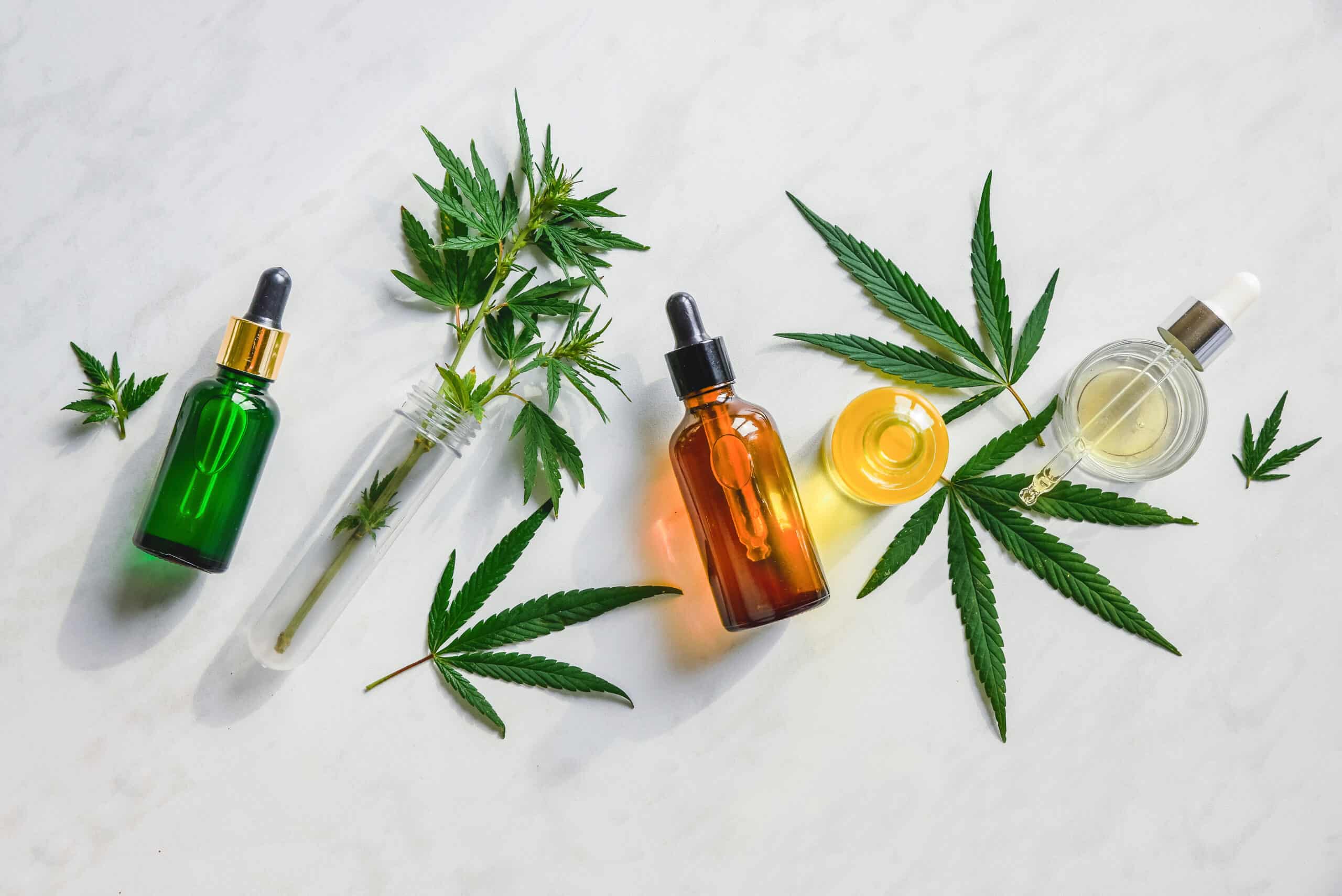 Different glass bottles with CBD OIL, THC tincture and cannabis leaves on yellow background. Flat lay, minimalism. Cosmetics CBD oil.