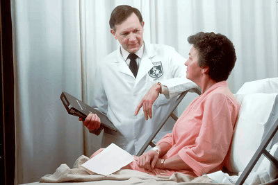 A doctor speaks to a woman patient who is seated on a hospital bed.