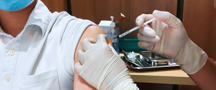 Asian man wear face mask receive Coronavirus vaccine injection jab by nurse or general practitioner at hospital or healthcare clinic service. People on vaccination or Covid-19 pandemic relief concept