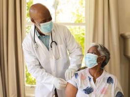 Senior african american woman and male doctor in face masks, woman receiving vaccination. retirement and senior lifestyle during covid 19 pandemic concept.