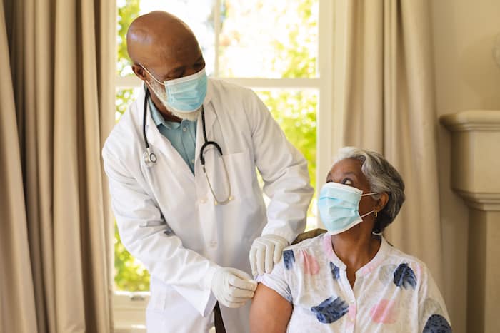 Senior african american woman and male doctor in face masks, woman receiving vaccination. retirement and senior lifestyle during covid 19 pandemic concept.