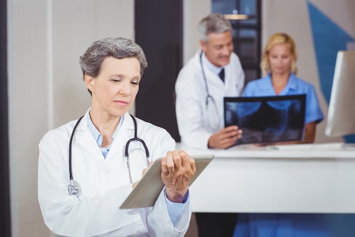 Female doctor using digital tablet with colleague checking X-ray at hospital