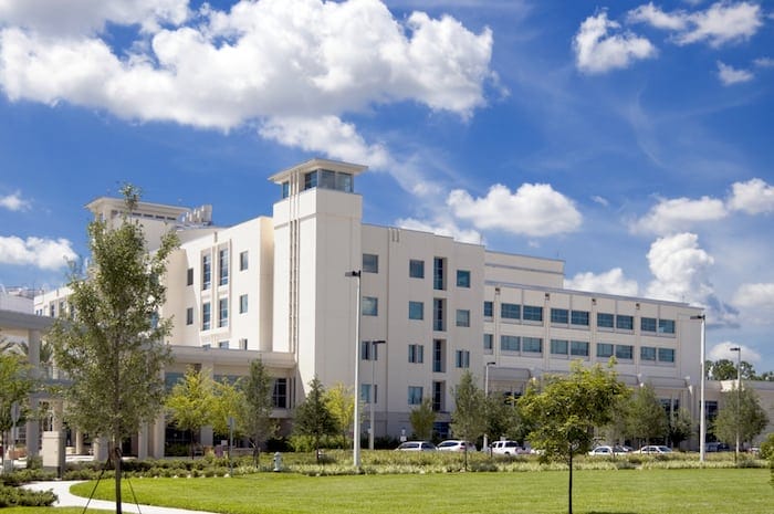 Front entrance to a hospital with palm tree landscaping and blue sky