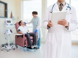Midsection of doctor holding digital tablet while nurse looking at patient being examined by heartbeat machine in hospital