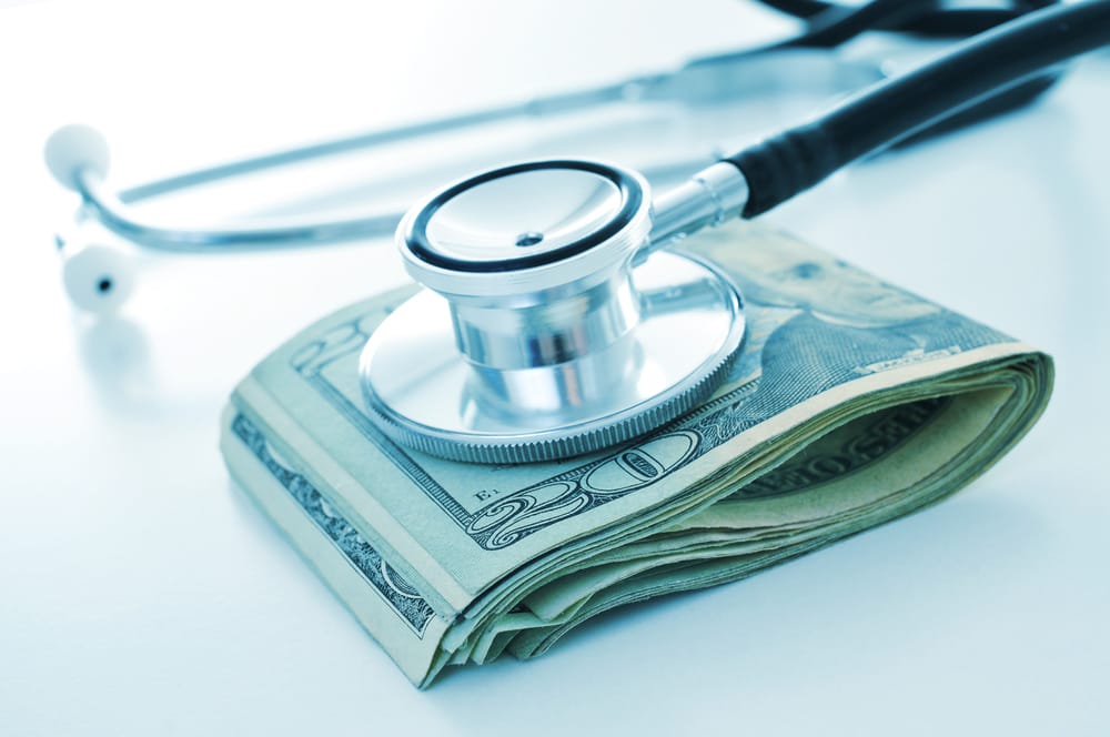 a stethoscope on a wad of US dollar bills, depicting the concepts of the health care industry or the health care costs