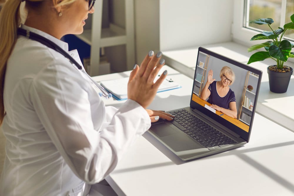 Telemedicine and e-health services. Closeup of doctor waving hand at computer screen greeting senior woman at online consultation. General practitioner using laptop to video call mature patient