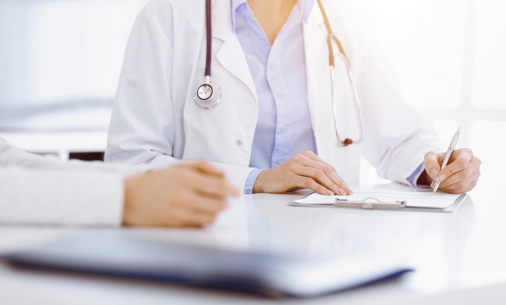 Unknown woman-doctor and female patient sitting and talking at medical examination in sunny clinic, close-up. Medicine concept