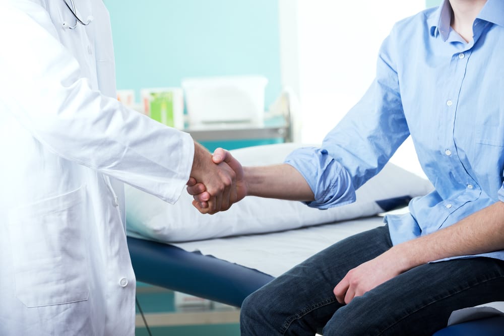 Doctor and patient handshake with medical equipment on the background.