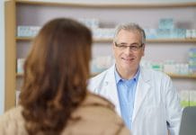 Attractive middle-aged male pharmacist standing listening to a female patient in the pharmacy, over the shoulder view of his face