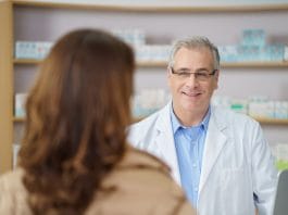 Attractive middle-aged male pharmacist standing listening to a female patient in the pharmacy, over the shoulder view of his face