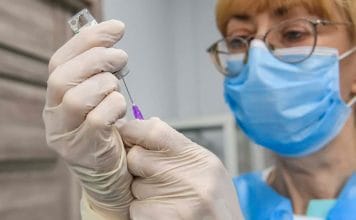 Medical worker in protective masks and gloves removes a dose of AstraZeneca Covishield coronavirus vaccine from a vial at a hospital