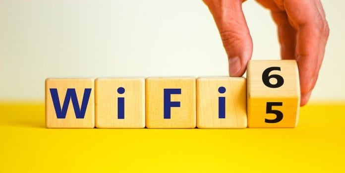 WiFi 5 or 6 symbol. Businessman turns a wooden cube and changes the words WiFi 5 to WiFi 6. Beautiful yellow, white background, copy space. Business, technology and WiFi 5 to WiFi 6 concept.