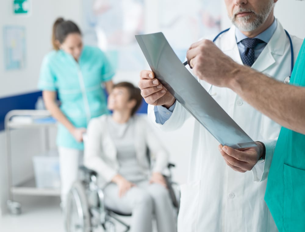 Confident professional doctors examining a patient's x-ray and woman on wheelchair helped by a nurse on the background