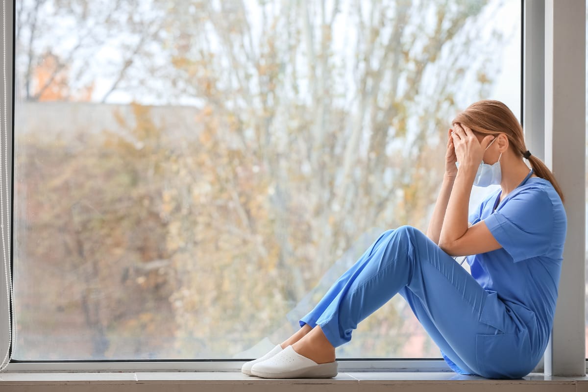 overworked nurse sitting down against the wall with hands over face