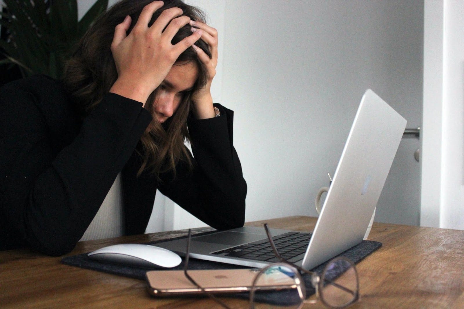 Woman grabbing her head in her hands looking distraught as she stares into her laptop