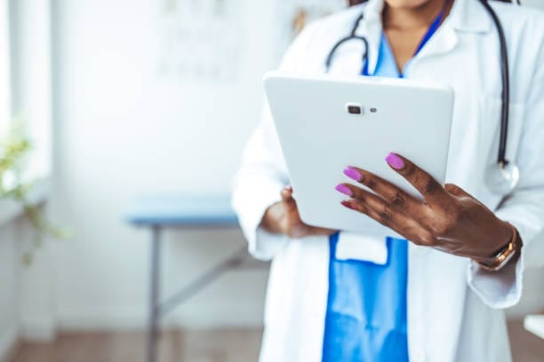 Close up of woman doctor hands using digital tablet at clinic. Closeup of female doctor in labcoat and stethoscope holding digital tablet, reading patient report. Hands holding medical report, copy space.