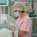 A female neonatal nurse treating a baby in the neonatal intensive care unit (NICU) of a hospital by checking its vitals.