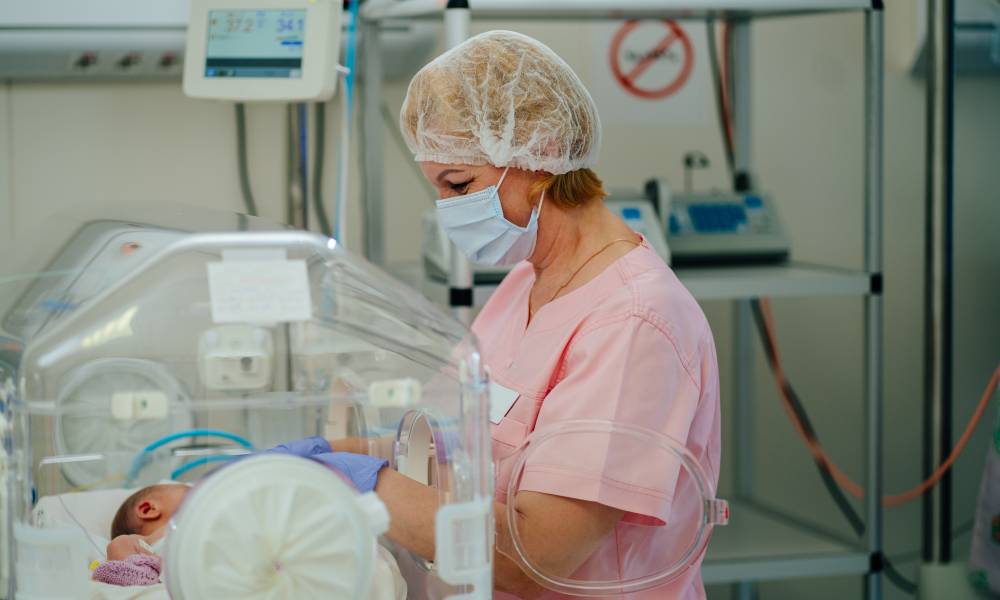 A female neonatal nurse treating a baby in the neonatal intensive care unit (NICU) of a hospital by checking its vitals.