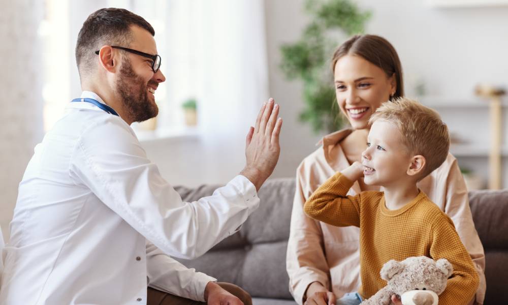 Family doctor about to high-five a child who has just had a checkup—the child is holding a stuffed bear.