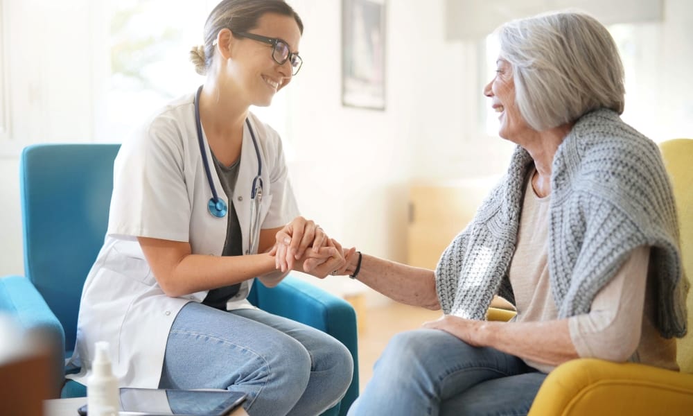 A doctor wearing a stethoscope around her neck talks to an older woman with a gray sweater around her shoulders.