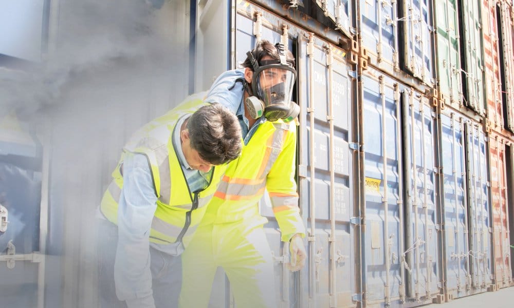 A worker wearing a respirator mask and high-visibility clothing carrying another person out of a smoky building.