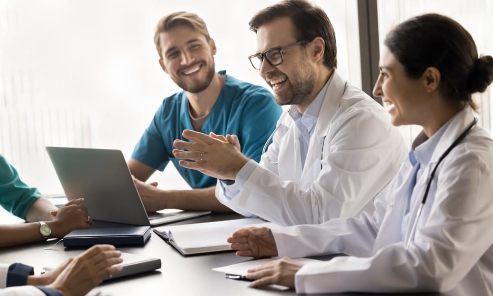 A group of medical professionals are talking and laughing during a team meeting. Each person has a huge smile on their face.