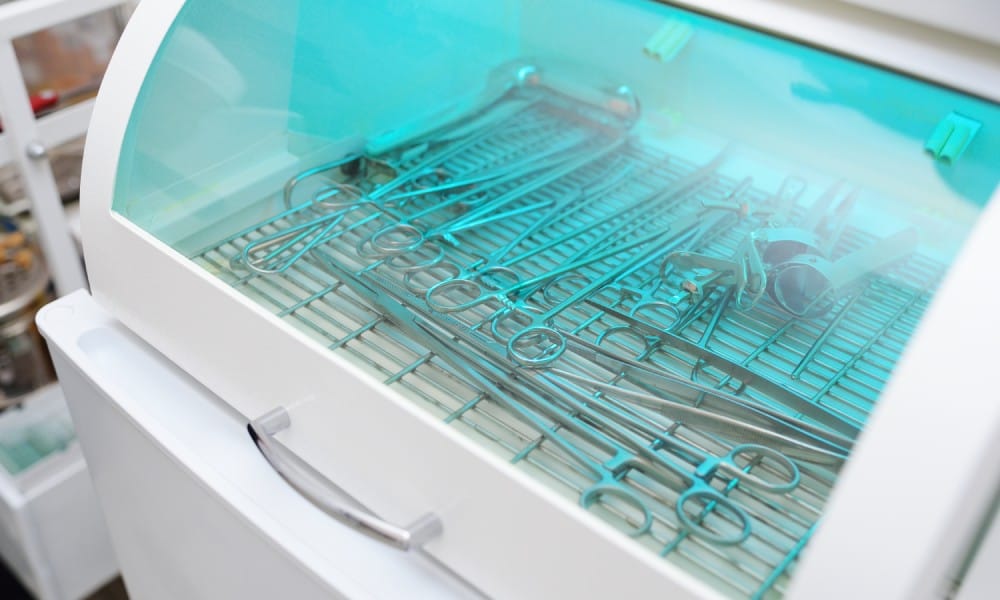 A sterilization machine emits blue light on medical instruments. There are multiple metallic forceps and other tools inside.