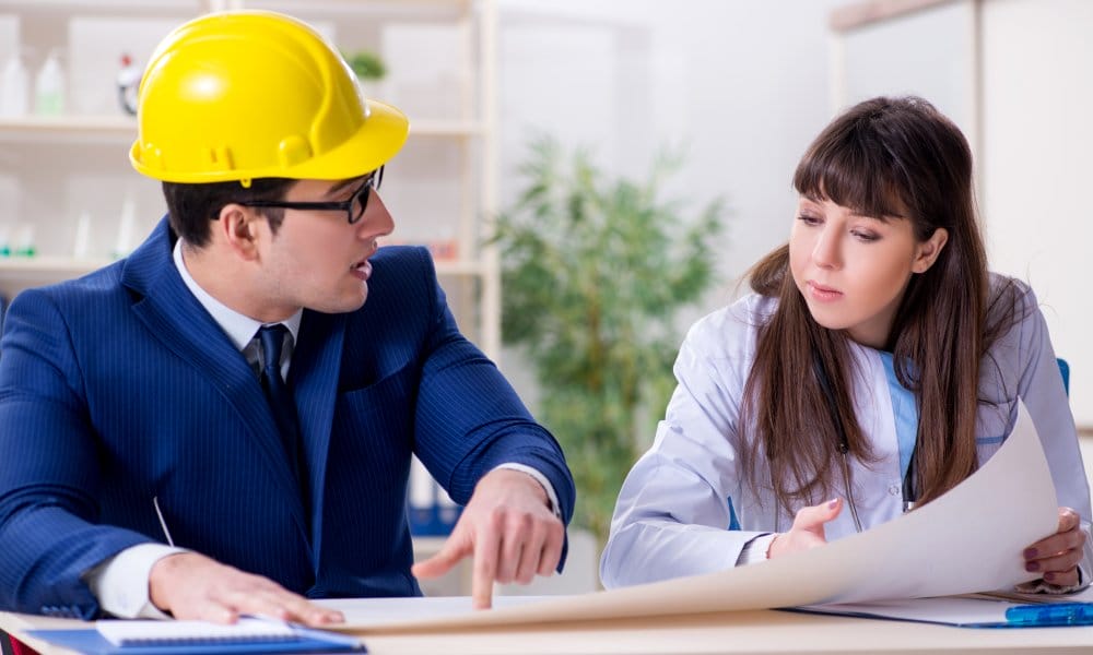 An architect and a doctor review blueprints for a construction project while sitting at a table indoors.