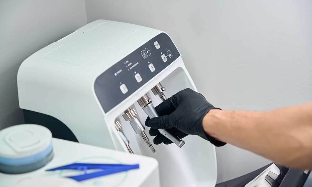 A person cleaning and setting up medical parts for a machine in a lab. Nearby is a tray of tools.