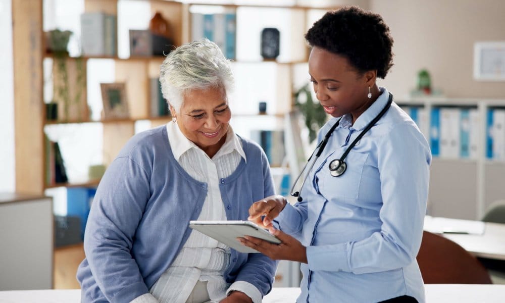 A medical practitioner and her patient sitting in a clinic while reviewing information on an electronic tablet.