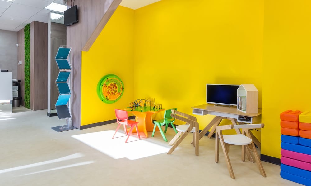 The waiting room of a facility has a desk, a computer on the far wall, and an area for children with colorful toys.