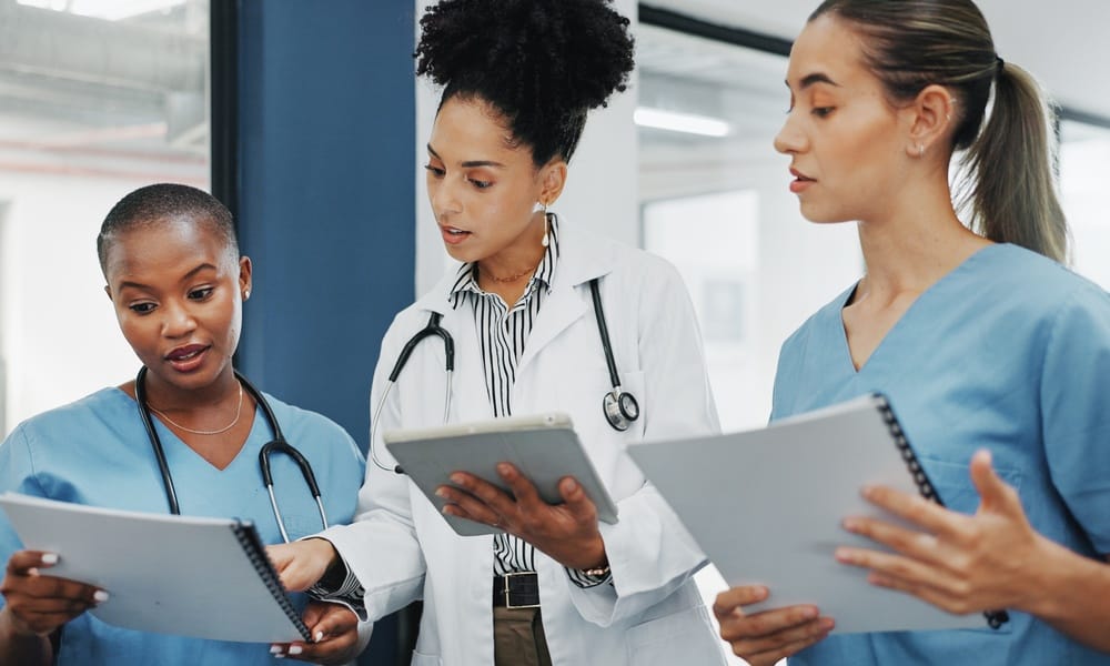 Two female nurses and a female doctor stand together in a clinic, reviewing paperwork and collaborating on patient care.