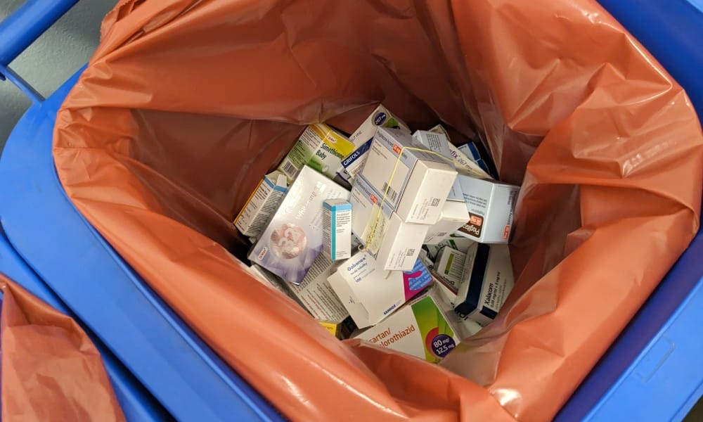 A overhead view of medication boxes and bottles in a blue disposal bin for hazardous pharmaceutical waste.