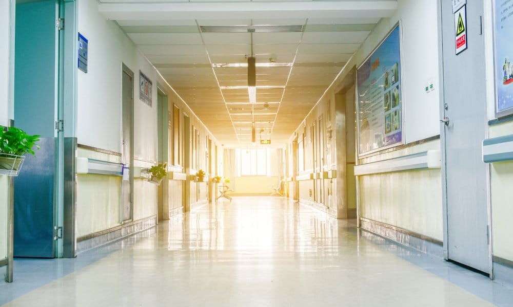 A hospital hallway contains several doors and openings. The sunshine comes through the window at the end of the hallway.