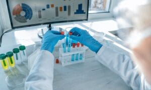 A lab professional wearing two blue latex gloves as they place fluid-filled vials into a lab sorting tray.