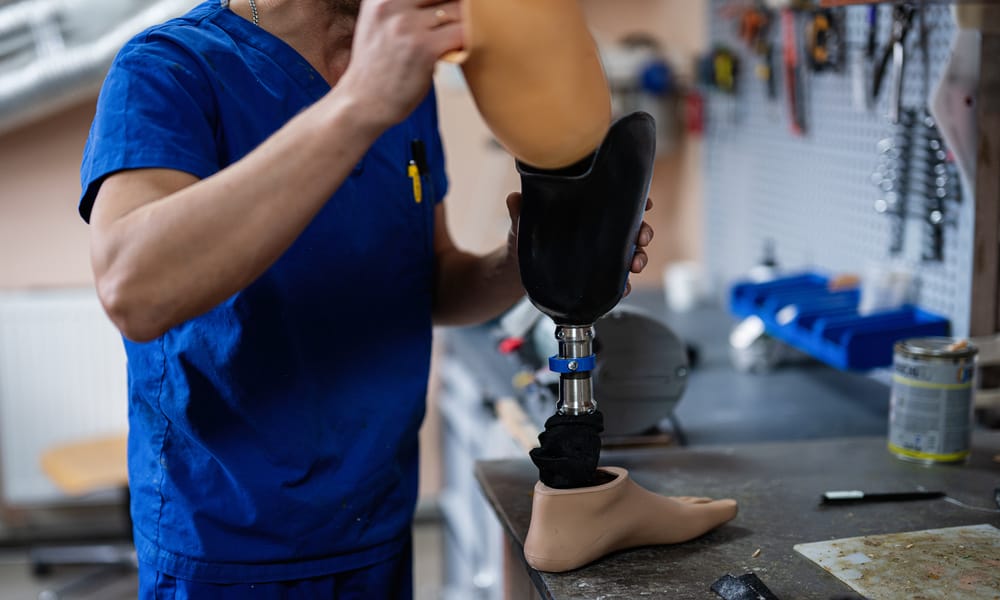 A medical professional assembles a prosthetic leg in an orthotics workshop and inspects its knee joint.