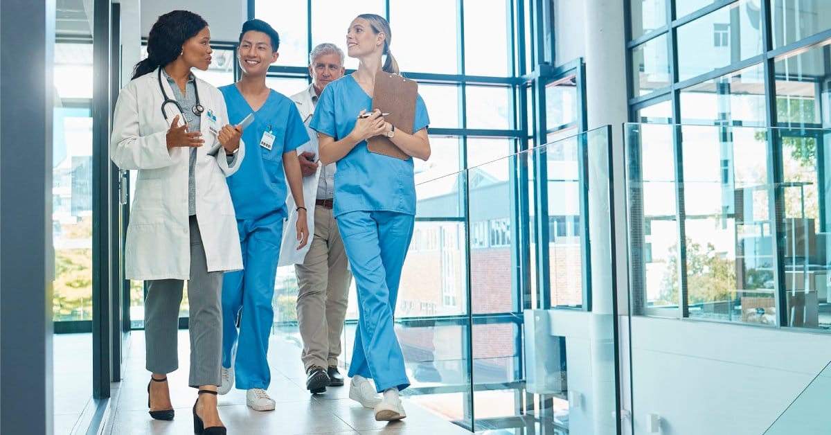 A mixed-gender group of healthcare workers walking in a large, clean facility with glass window walls.