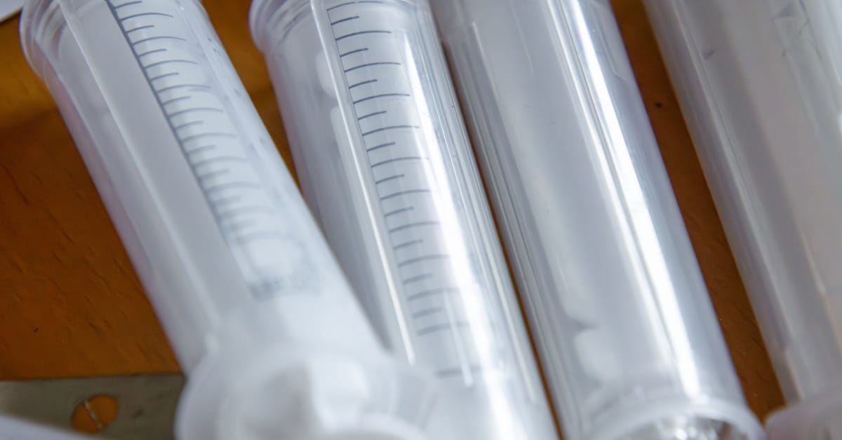 A collection of translucent plastic syringes with markings lying haphazardly in a row on a wooden surface.