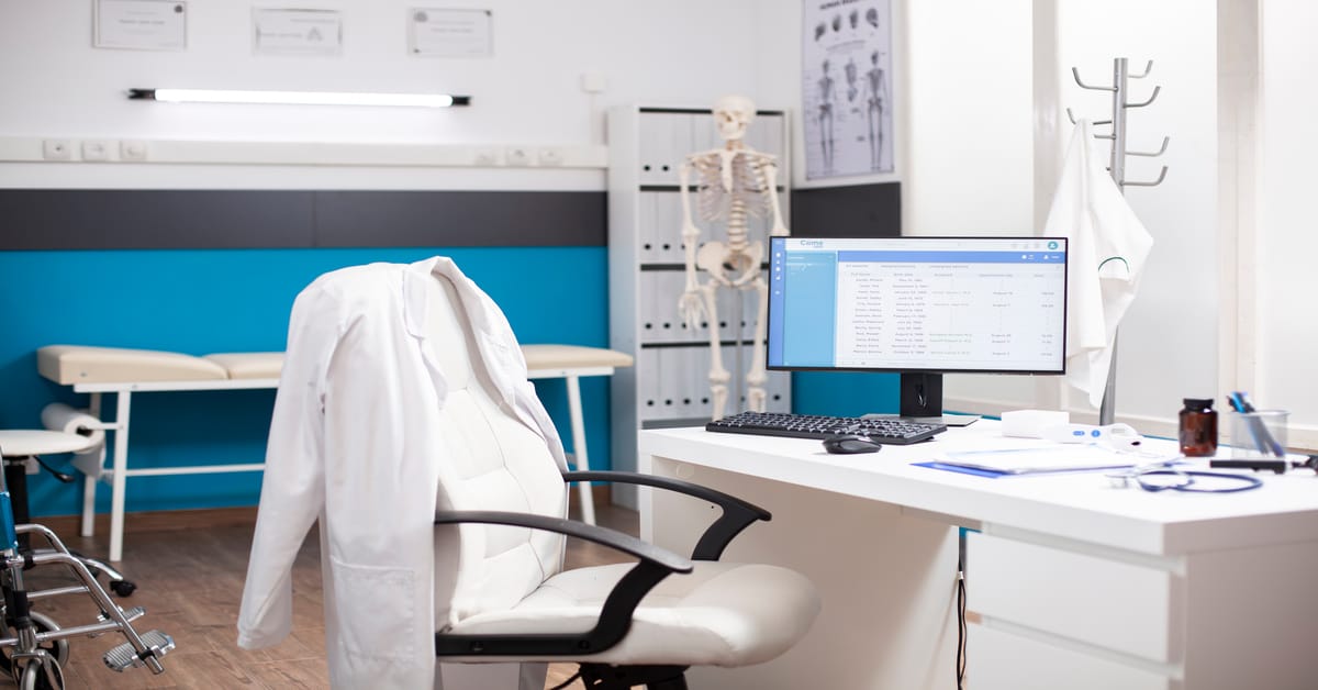 Modern medical office shows empty exam room with clinical tools and a desktop displaying diagnostic data.