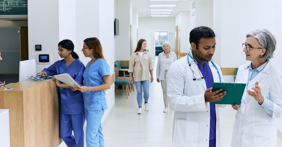 A panoramic view of a hospital corridor filled with nurses, doctors, and visitors. They are walking and talking.