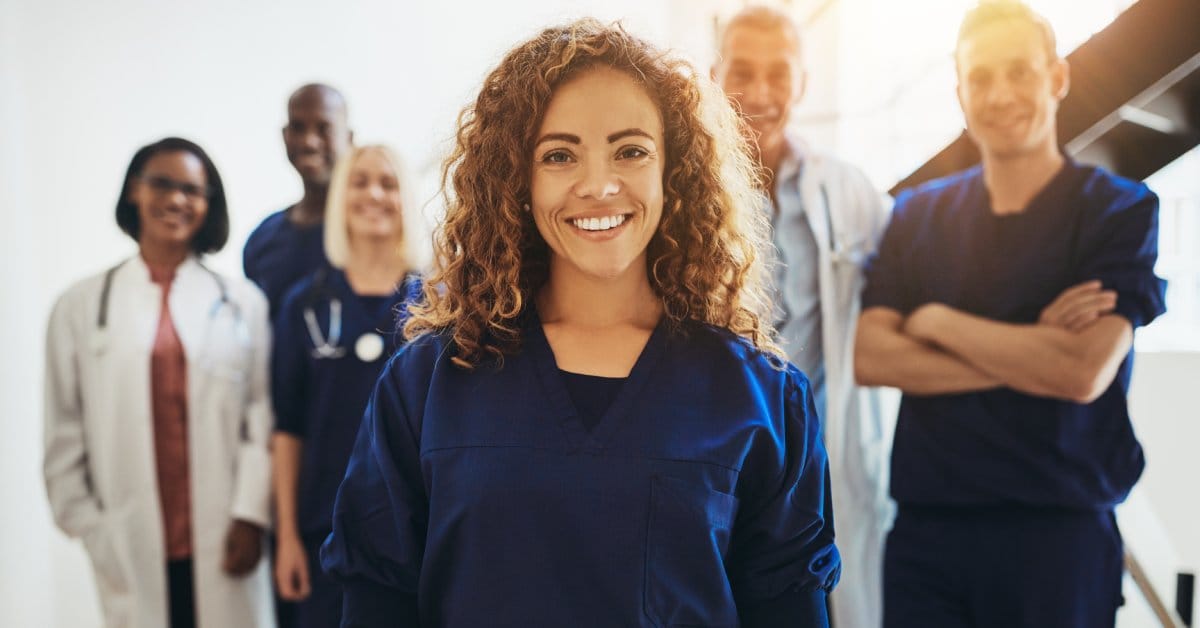 A close-up of a smiling woman doctor standing with a diverse group of medical colleagues in a hospital.