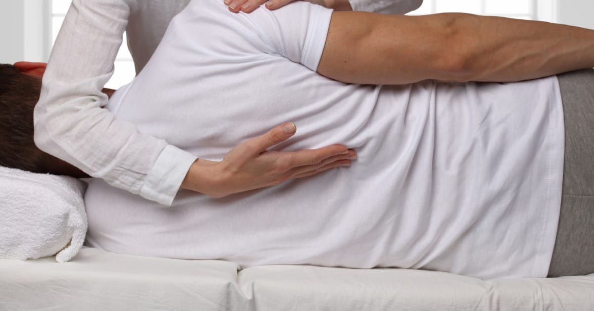 A chiropractor performs a spinal adjustment on a patient who is lying on their side on a medical exam table.