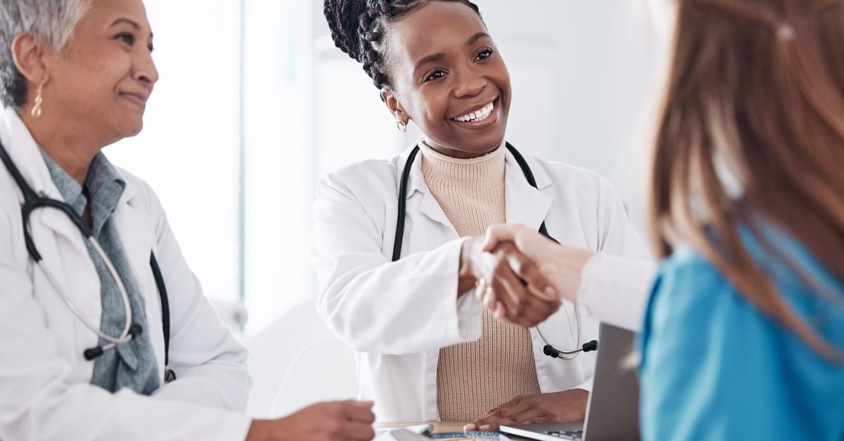 Two doctors interviewing a person. One of the doctors is smiling and shaking hands with the interviewee.